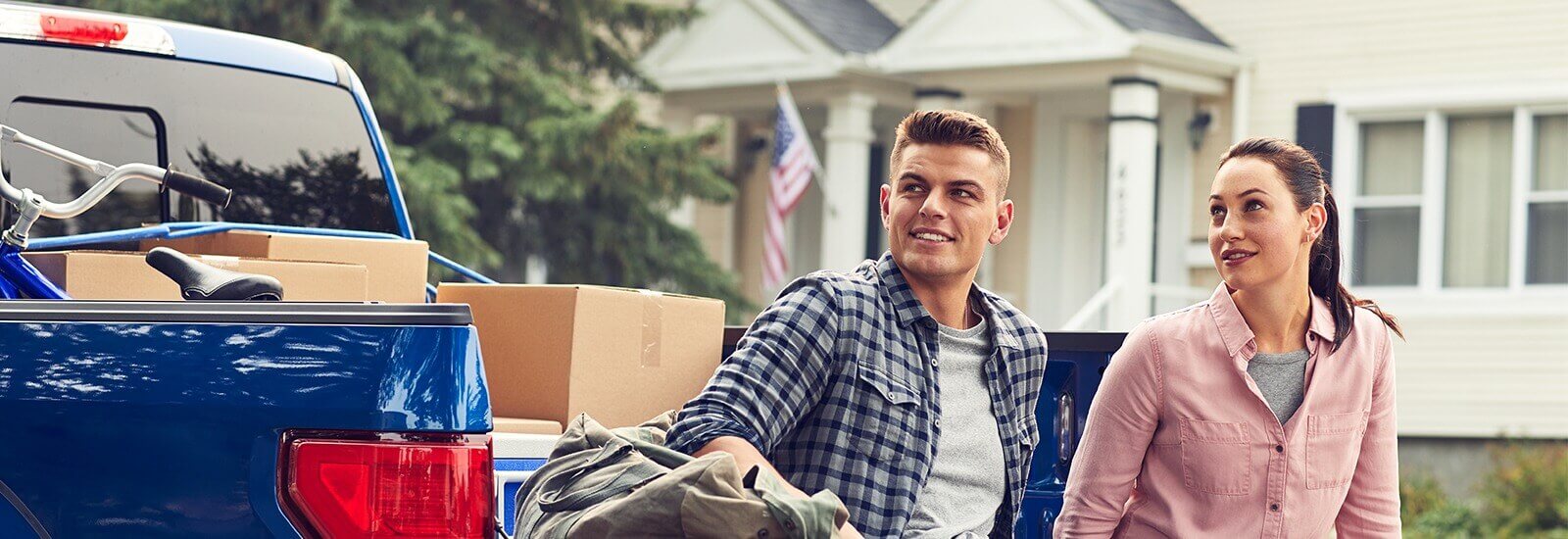 A smiling married couple sitting on the back of their new truck they purchased