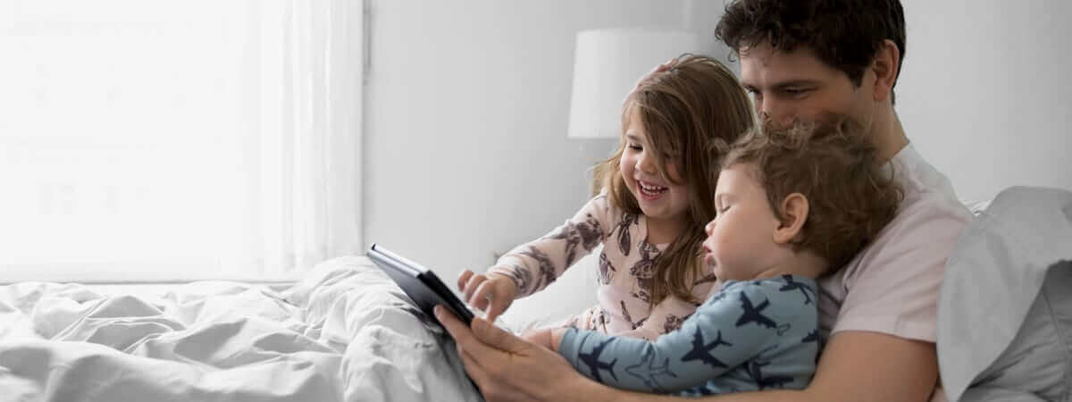 A father is reading a story to his two small children while laying in bed