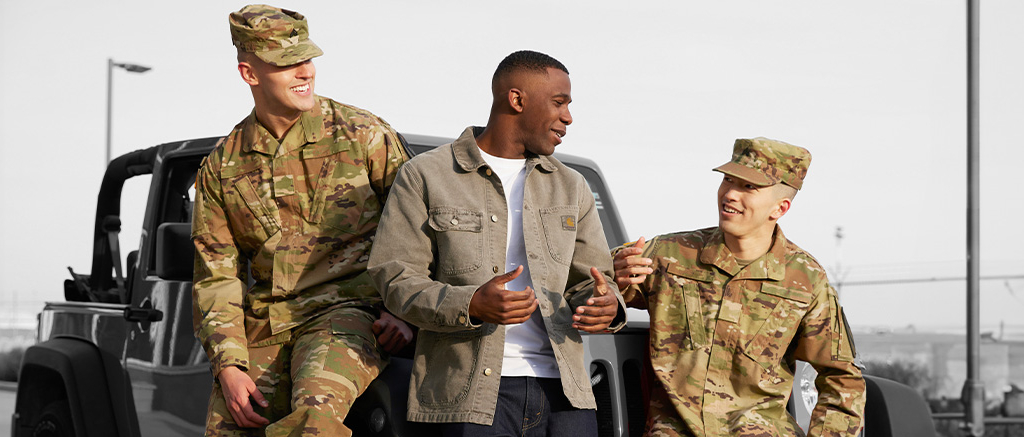 Three early-career military members sitting on a jeep talking.