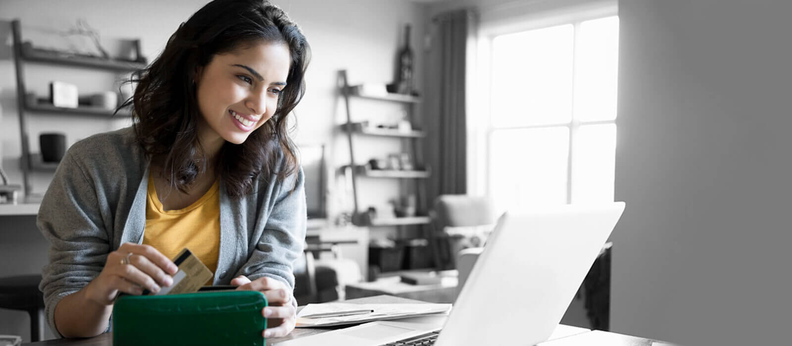 Woman looking at a laptop smiling, while putting a credit card into her wallet.