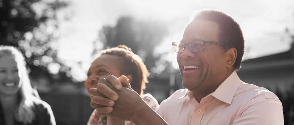 Older man in glasses sitting outside with other people.