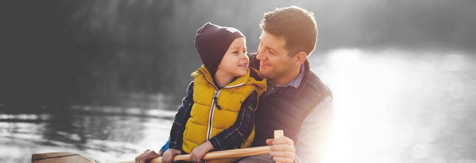 A parent and their child kayaking together on a lake during a bright sunny day