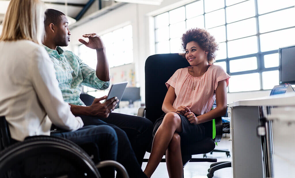 Three employees chatting about a project inside their bright and spacious office